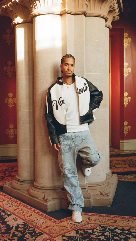 Man in stylish outfit standing in an ornate room with red walls and gold patterns.